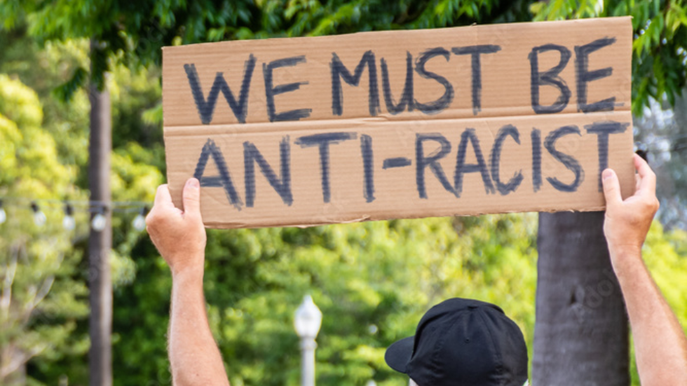 Adult holding up a "We Must be Anti-Racist" cardboard sign 